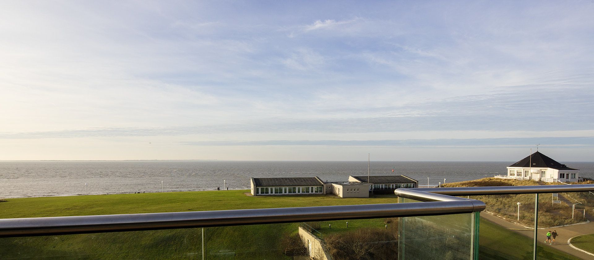 A coastal view with a grassy area, a small building, and a larger white structure with a black roof.