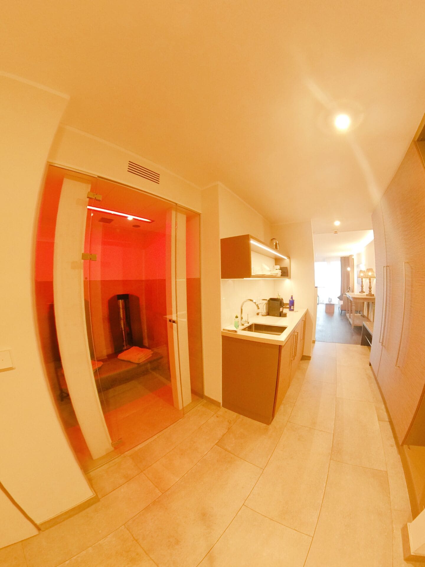 A modern kitchen with a built-in oven, a sink, and a countertop with cabinets. There is a glass door leading to a separate room.