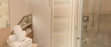 A modern bathroom with a glass shower enclosure, a vanity with a mirror, and a towel stack.