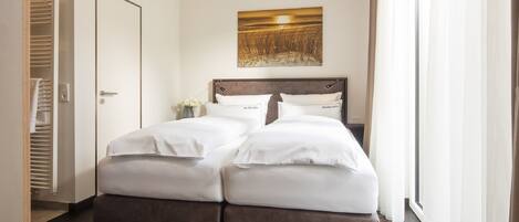 Una cama doble con sábanas blancas, cabecera de madera y un cuadro de un atardecer en la pared.