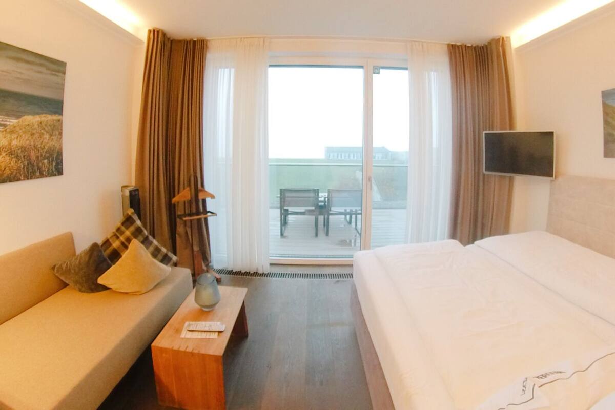 Habitación de hotel con cama, sofá, televisión y balcón con vistas.