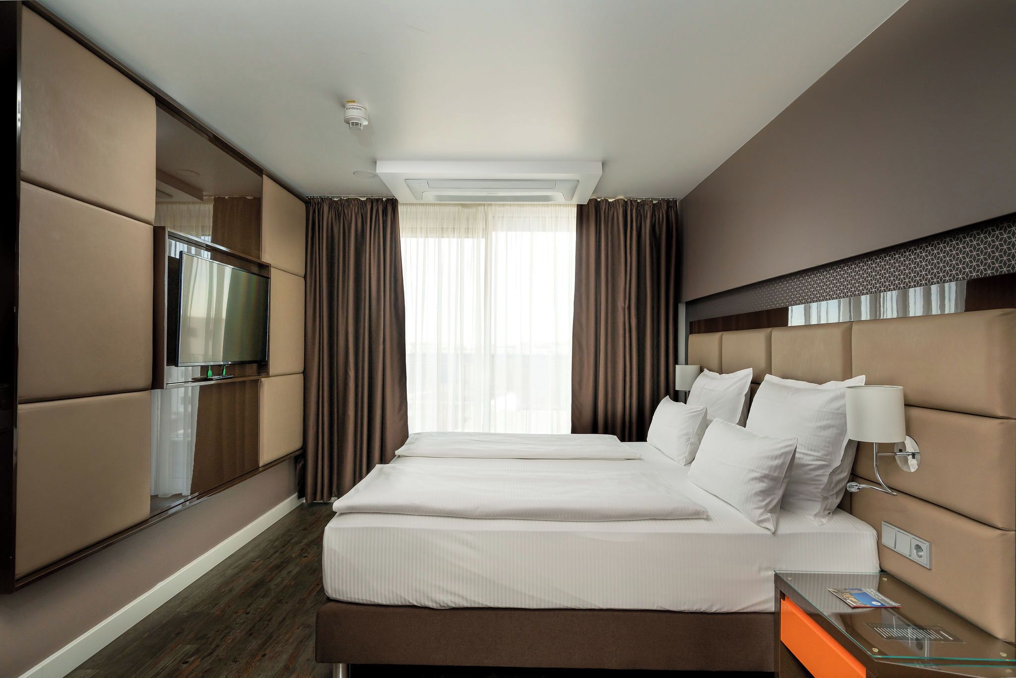 A hotel room with a large bed, a TV, and a minibar.