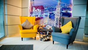 Two armchairs with yellow and grey cushions, a small round table with decorative eggs, and a cityscape view through a window. - Kreis Residenz München (Munich)