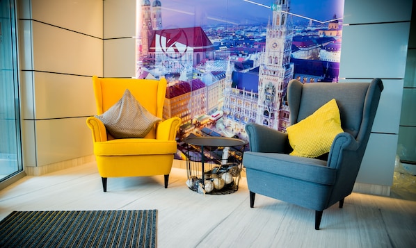 Dos sillones con cojines amarillos y grises, una mesita redonda con huevos decorativos y vista a un paisaje urbano a través de una ventana.