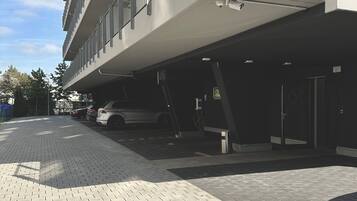 Een modern gebouw met een parkeergarage, een verharde looppad en een witte auto die er geparkeerd staat.