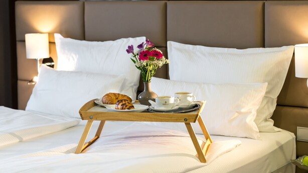 A neatly made bed with white linens, a tray with croissants and coffee cups, and a vase with flowers. - Kreis Residenz München (Munich)
