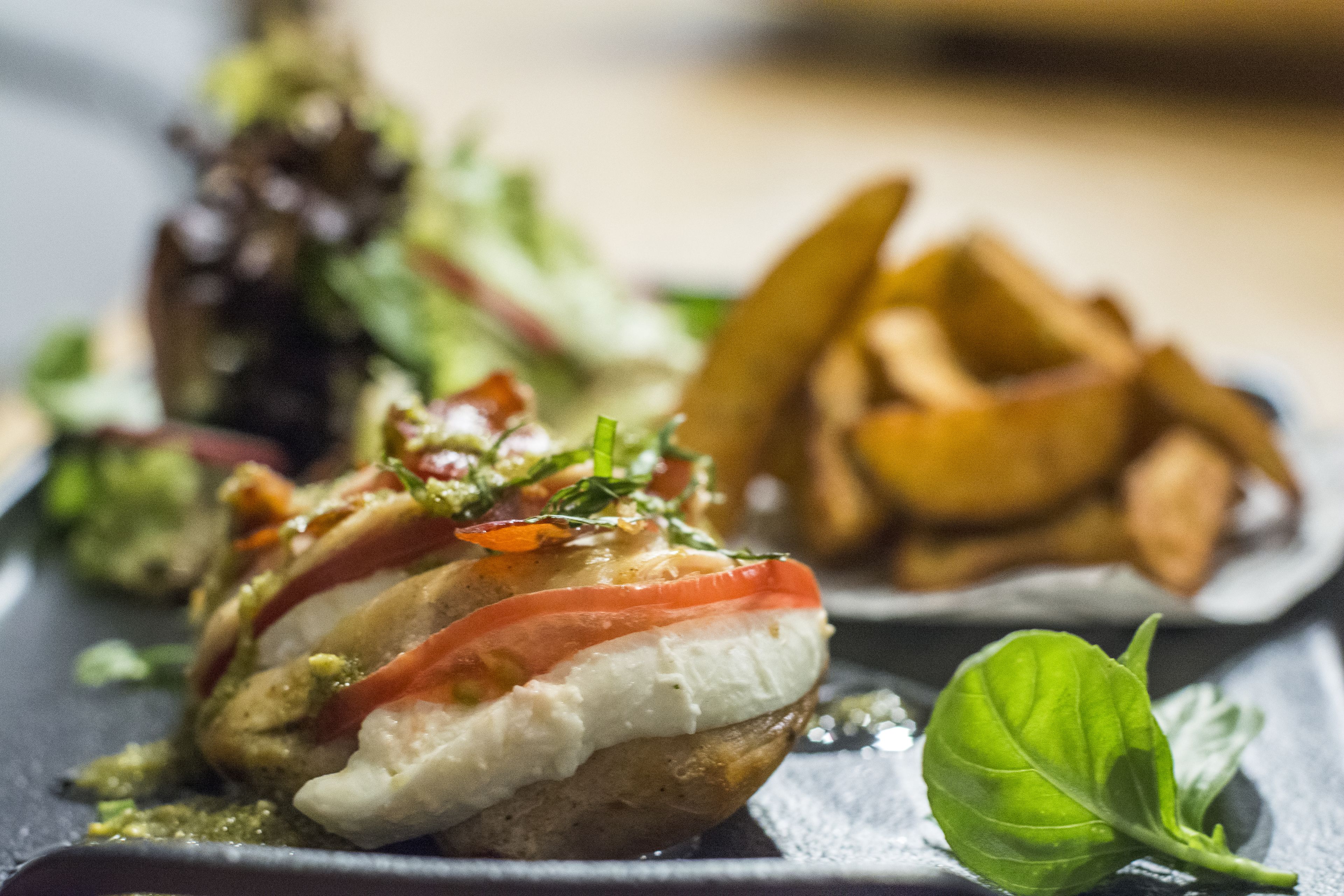 A dish with a creamy topping, tomato slices, and a basil leaf on a plate.