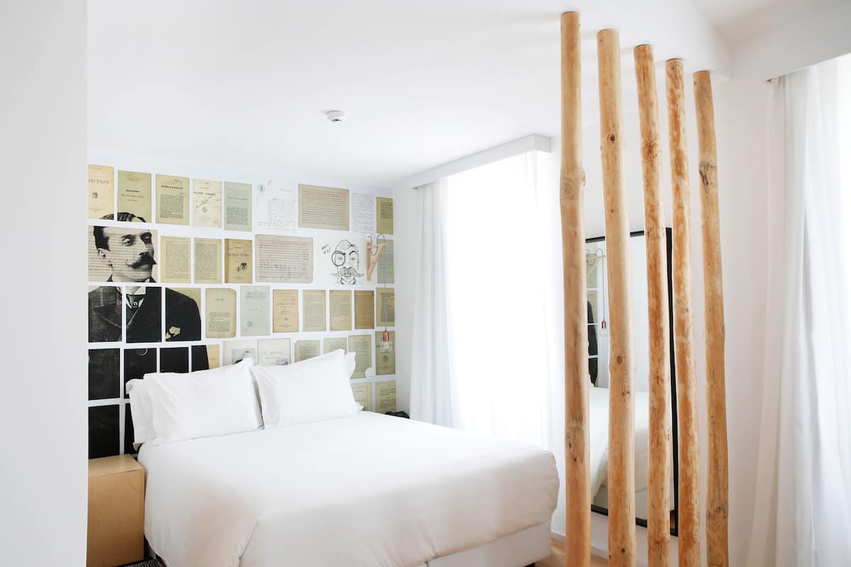Une chambre à coucher avec un lit, un mur décoré de différents papiers et une fenêtre avec des rideaux.