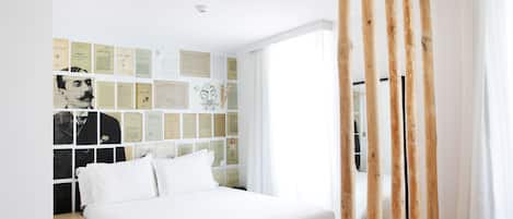 A bedroom with a bed, a wall decorated with various papers, and a window with curtains.