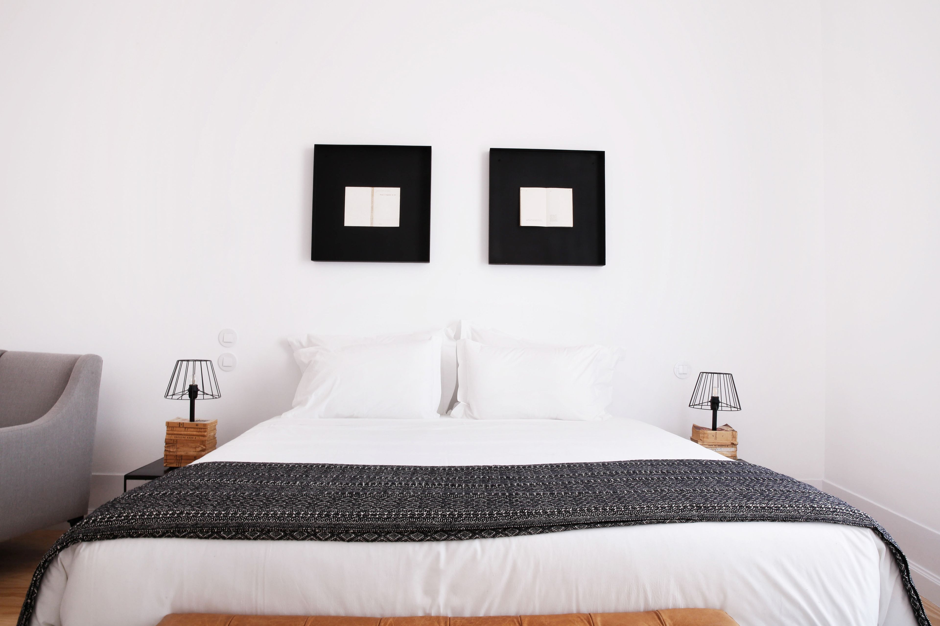 A neatly arranged bedroom with a large bed, two bedside tables with lamps, a grey armchair, and two framed pictures on the wall.