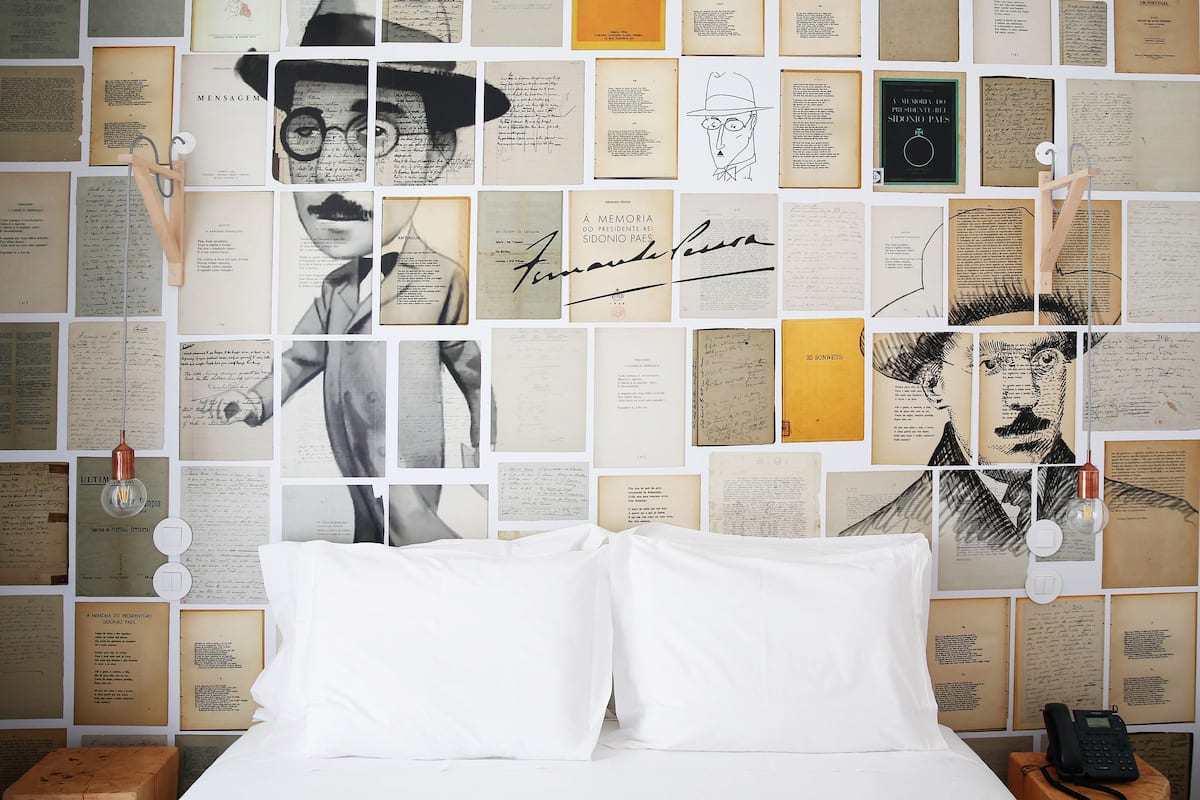 Une chambre à coucher avec un lit, des oreillers blancs et un mur recouvert de divers documents et photographies.