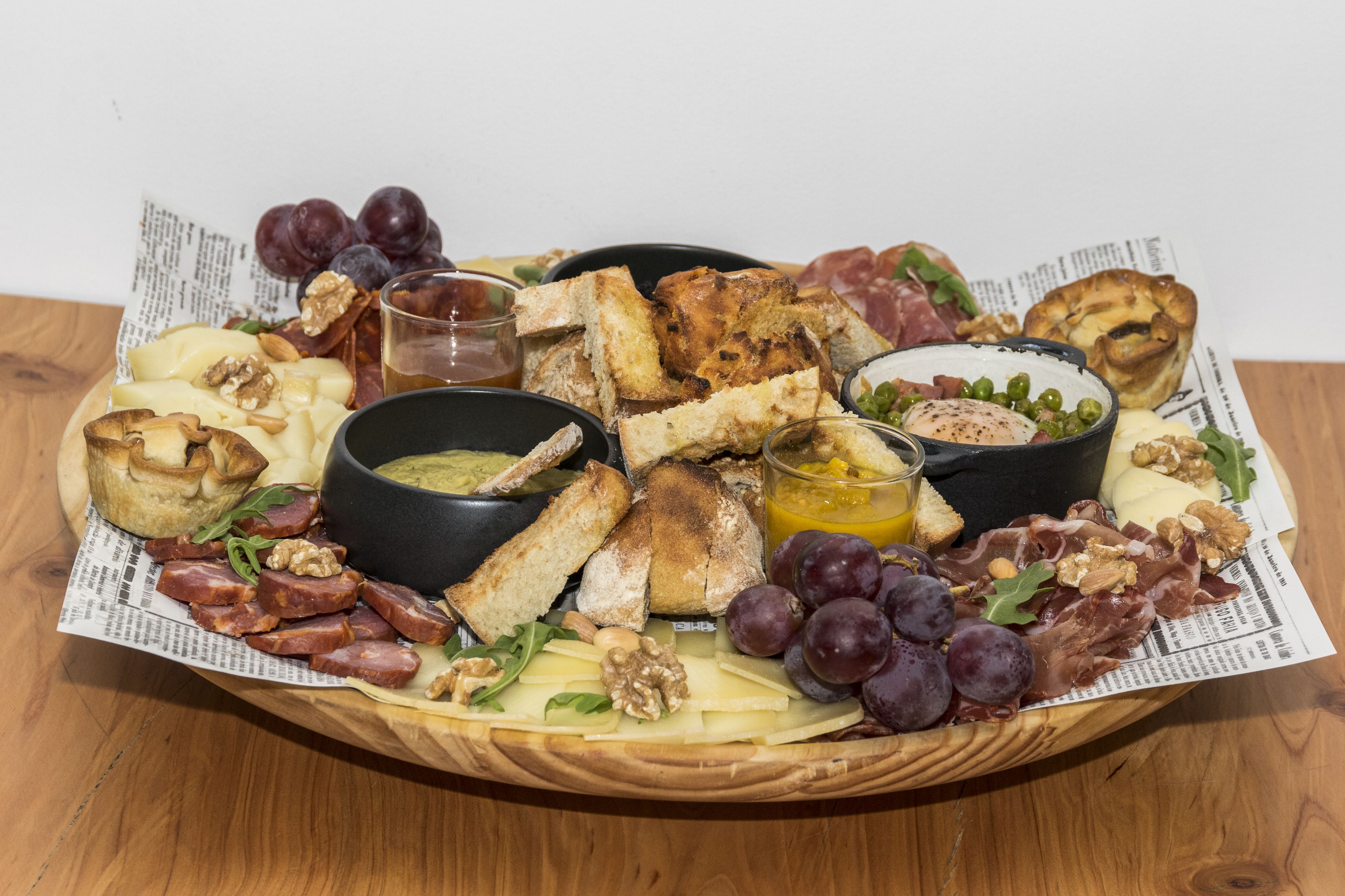 Une planche de charcuterie comprenant divers fromages, viandes, fruits et fruits secs, le tout disposé sur une planche en bois.