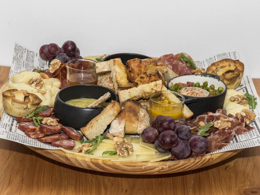 Une planche de charcuterie comprenant divers fromages, viandes, fruits et fruits secs, le tout disposé sur une planche en bois.