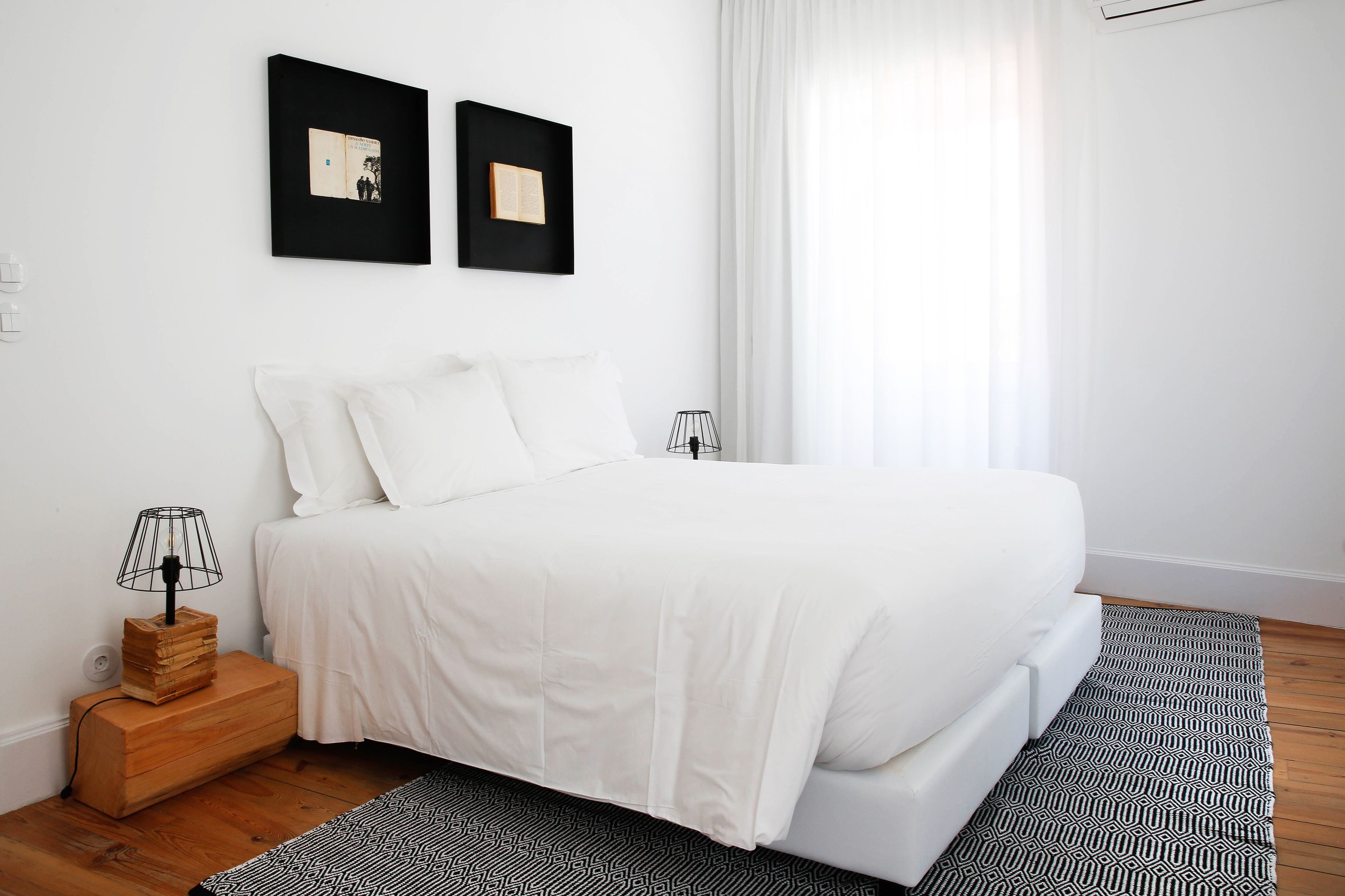 Un dormitorio ordenado con una cama grande, una mesita de noche con lámpara y dos cuadros en la pared.