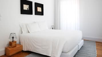 Un dormitorio ordenado con una cama grande, una mesita de noche con lámpara y dos cuadros en la pared.