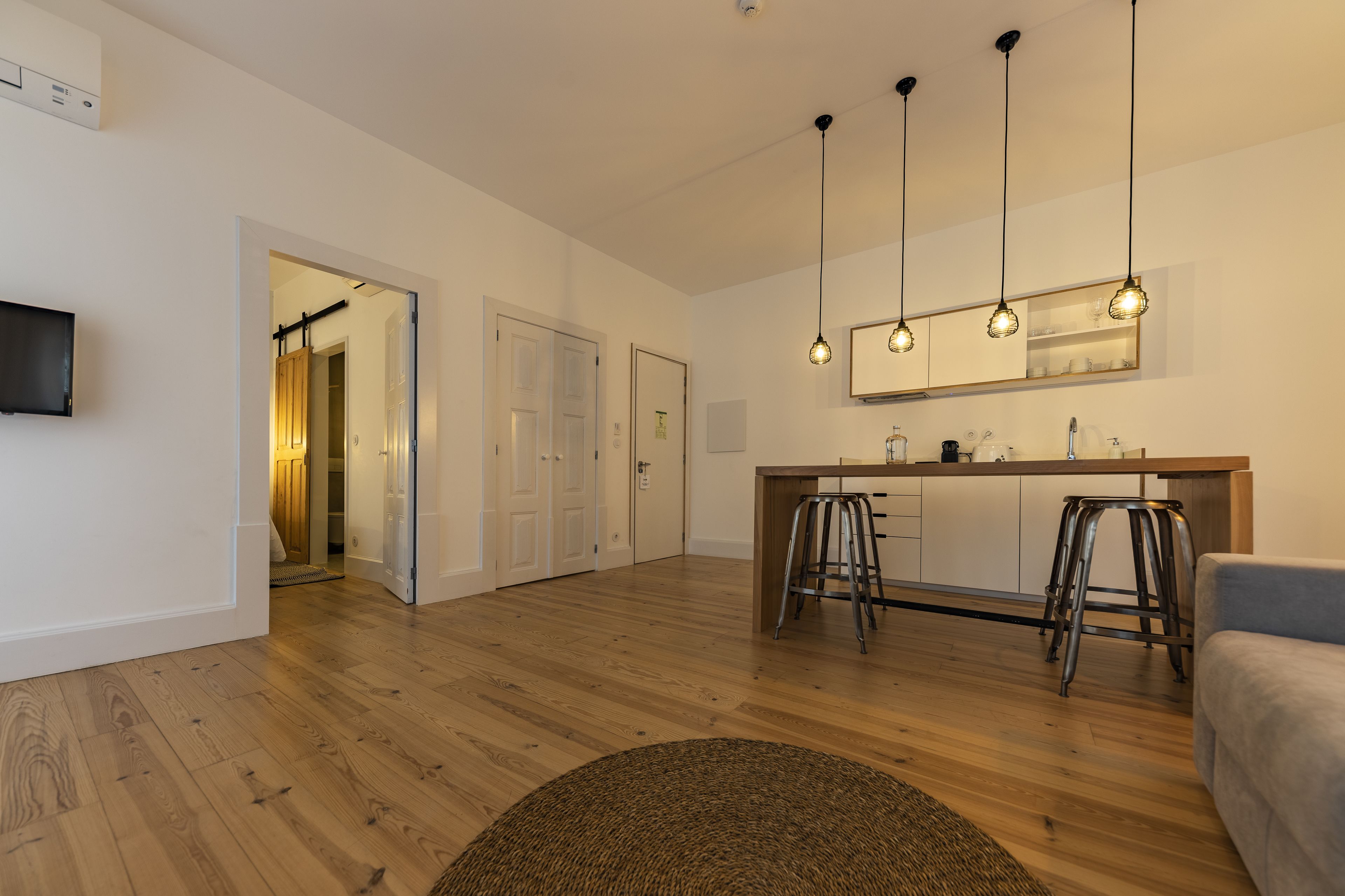 Una cocina moderna con suelo de madera, una zona de bar con taburetes y un televisor de pantalla plana montado en la pared.