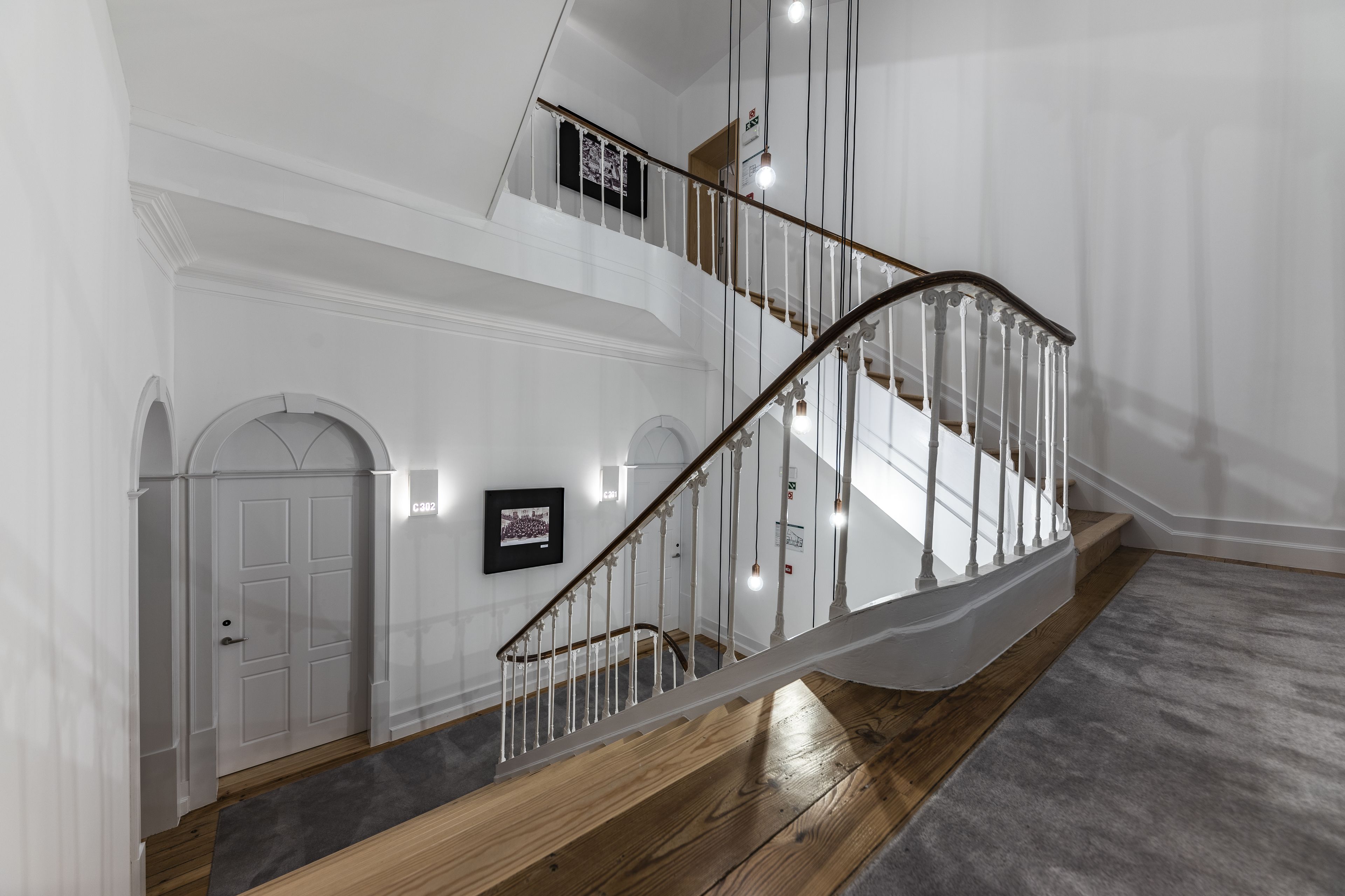 A modern staircase with a wooden finish and white railings, leading to an upper floor with white walls and a door.
