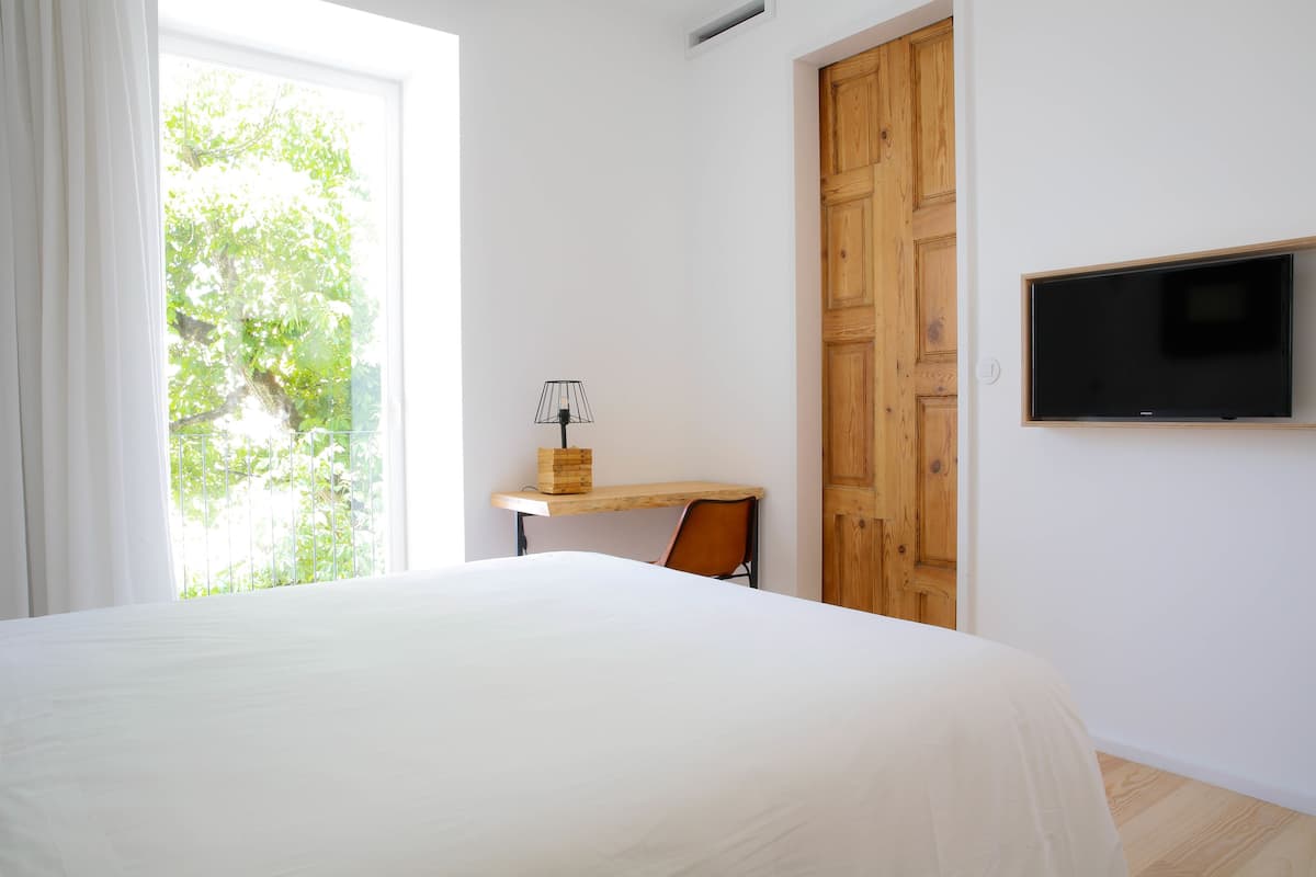 Une chambre à coucher avec un lit, un bureau, une chaise, un téléviseur et une fenêtre avec des rideaux.
