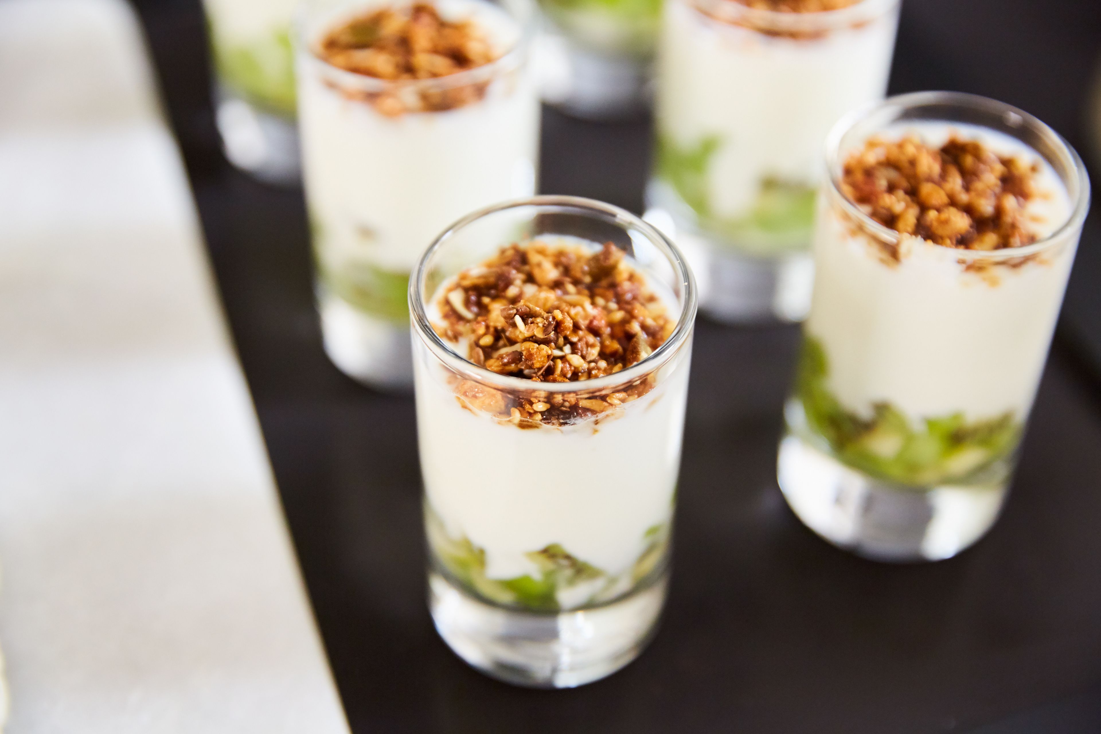 Four glasses of layered dessert with granola on top.