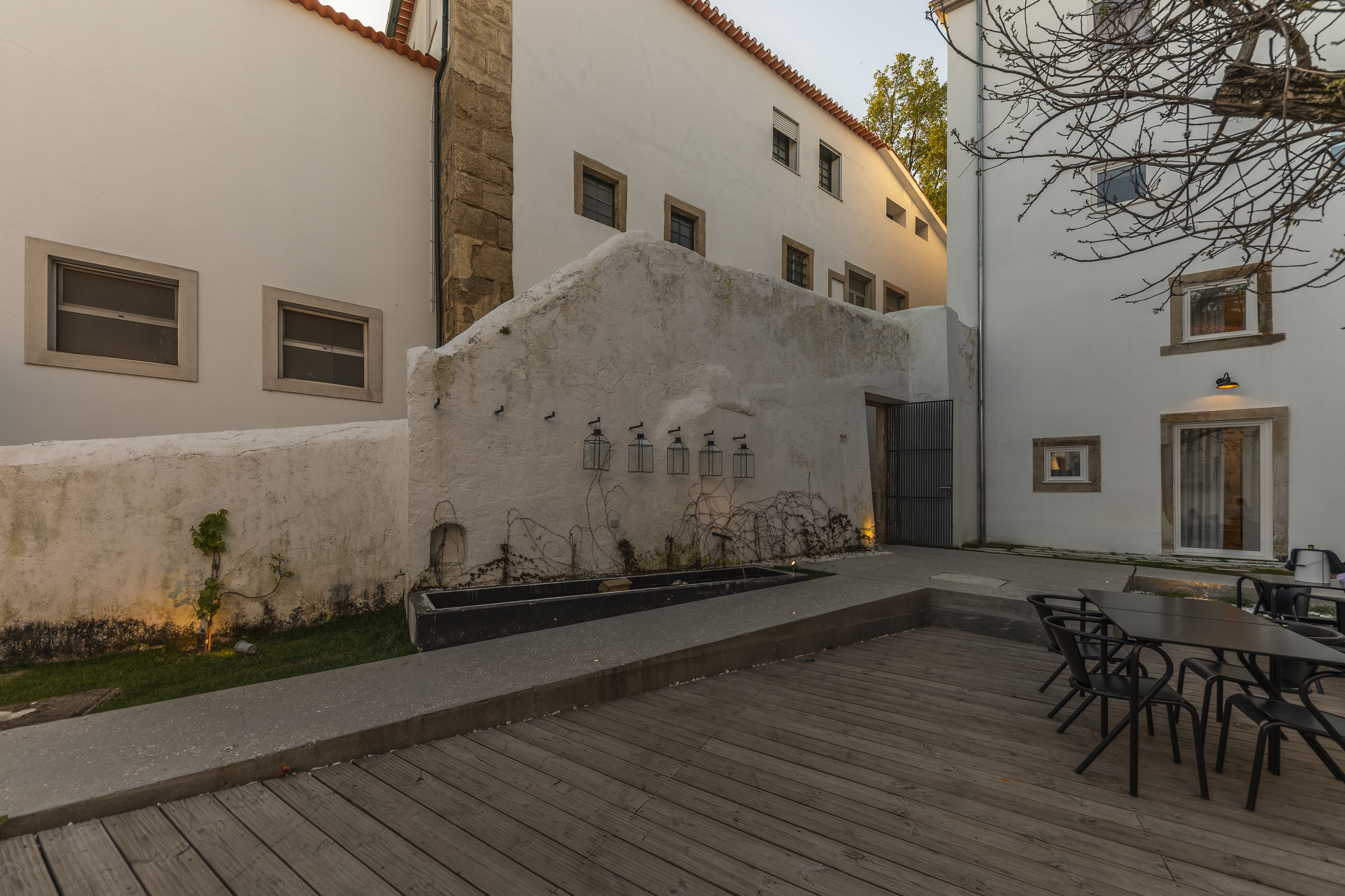 Un pati amb un pont de fusta, mobiliari exterior i un edifici blanc amb nombroses finestres i una paret de pedra.