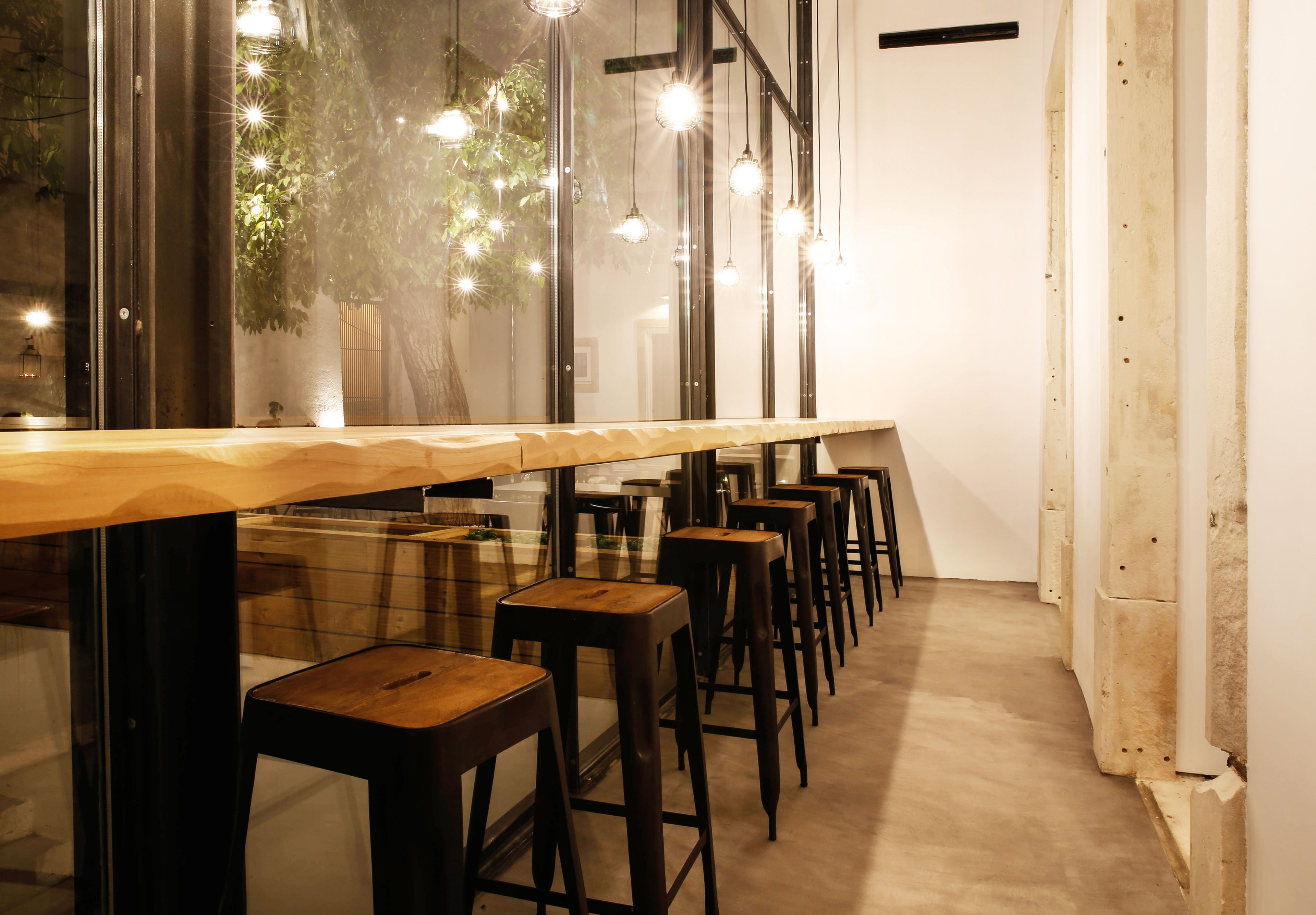 A long wooden table with multiple barstools, large windows, and hanging light fixtures.