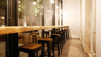 A long wooden table with multiple barstools, large windows, and hanging light fixtures.