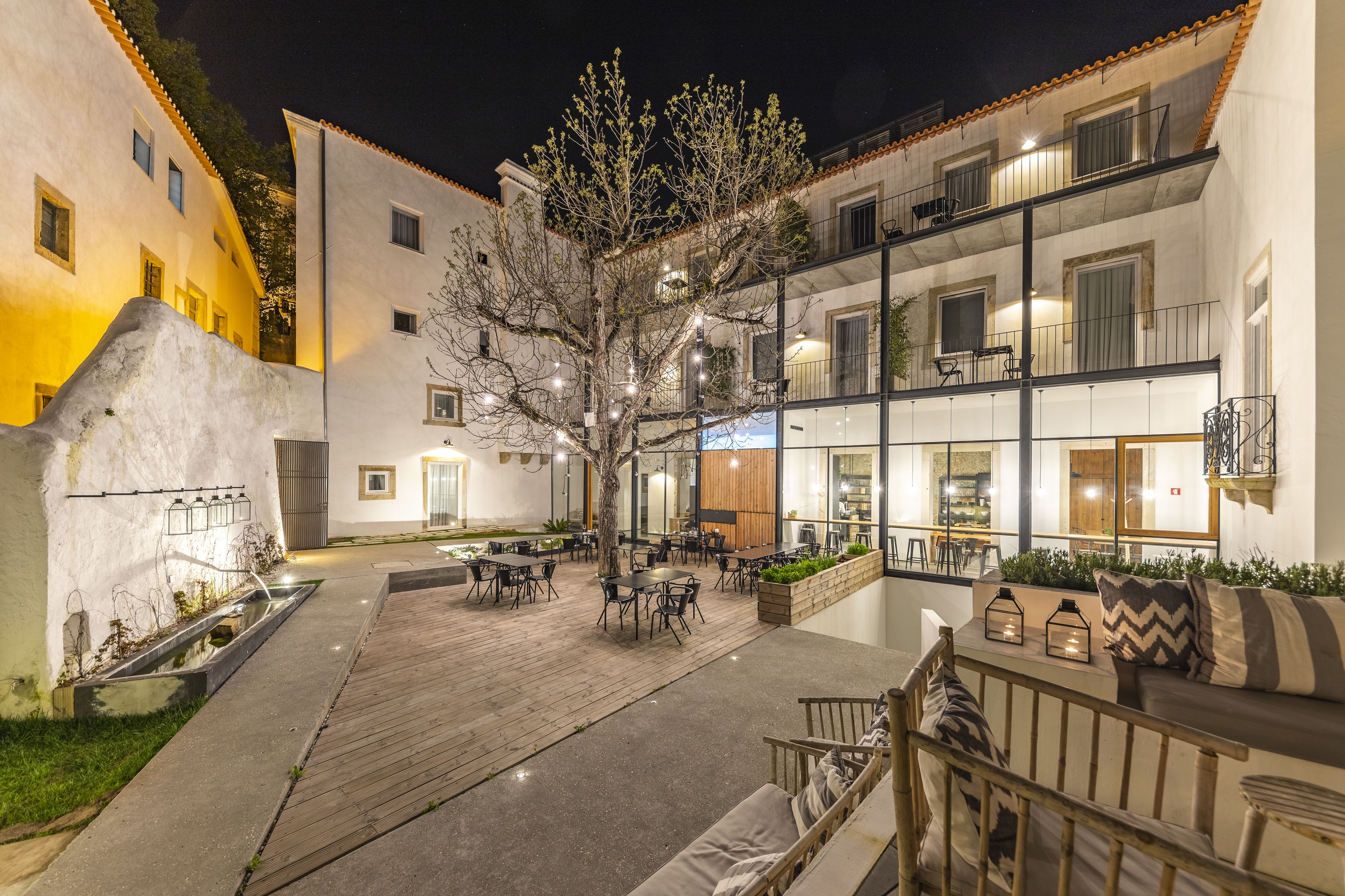 A courtyard with outdoor seating, a tree, and a building with multiple floors and balconies.
