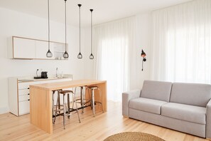 Un espace de vie moderne avec une table à manger en bois, des tabourets de bar, un canapé gris et des luminaires suspendus.