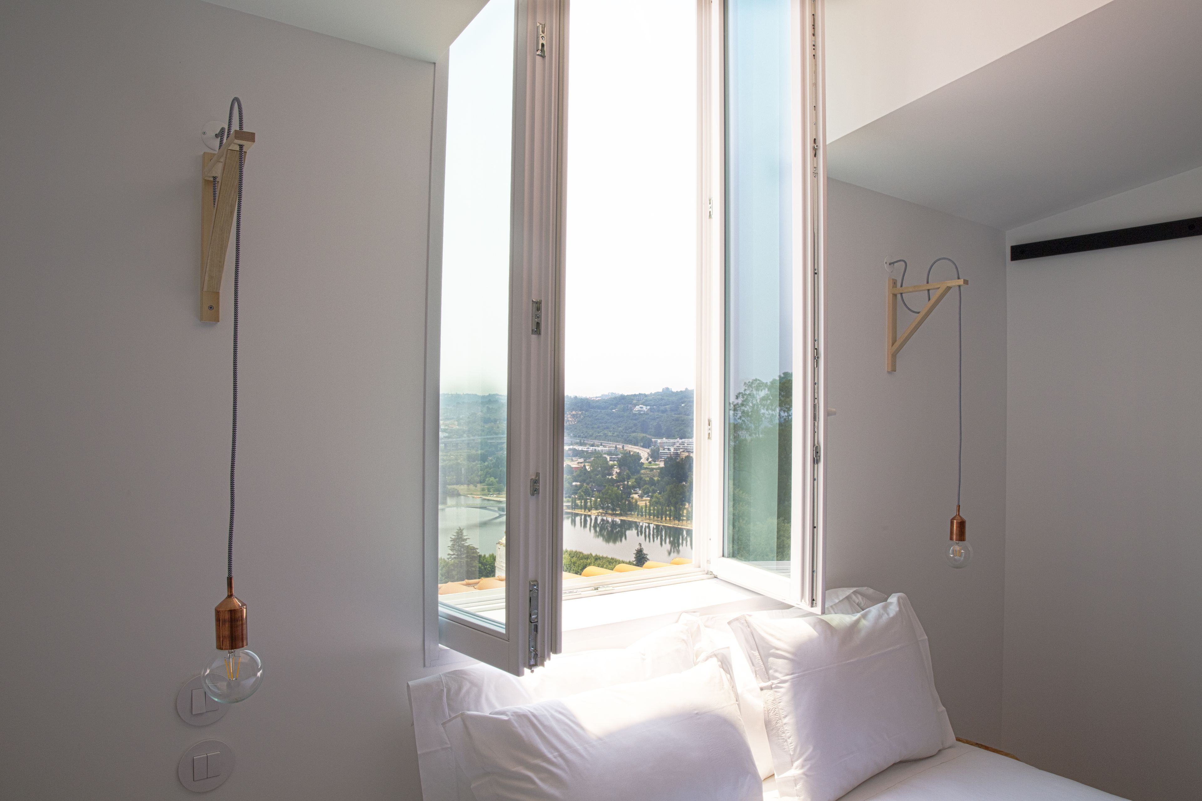 A bedroom with a large window, a bed, and a view of a bridge and landscape.