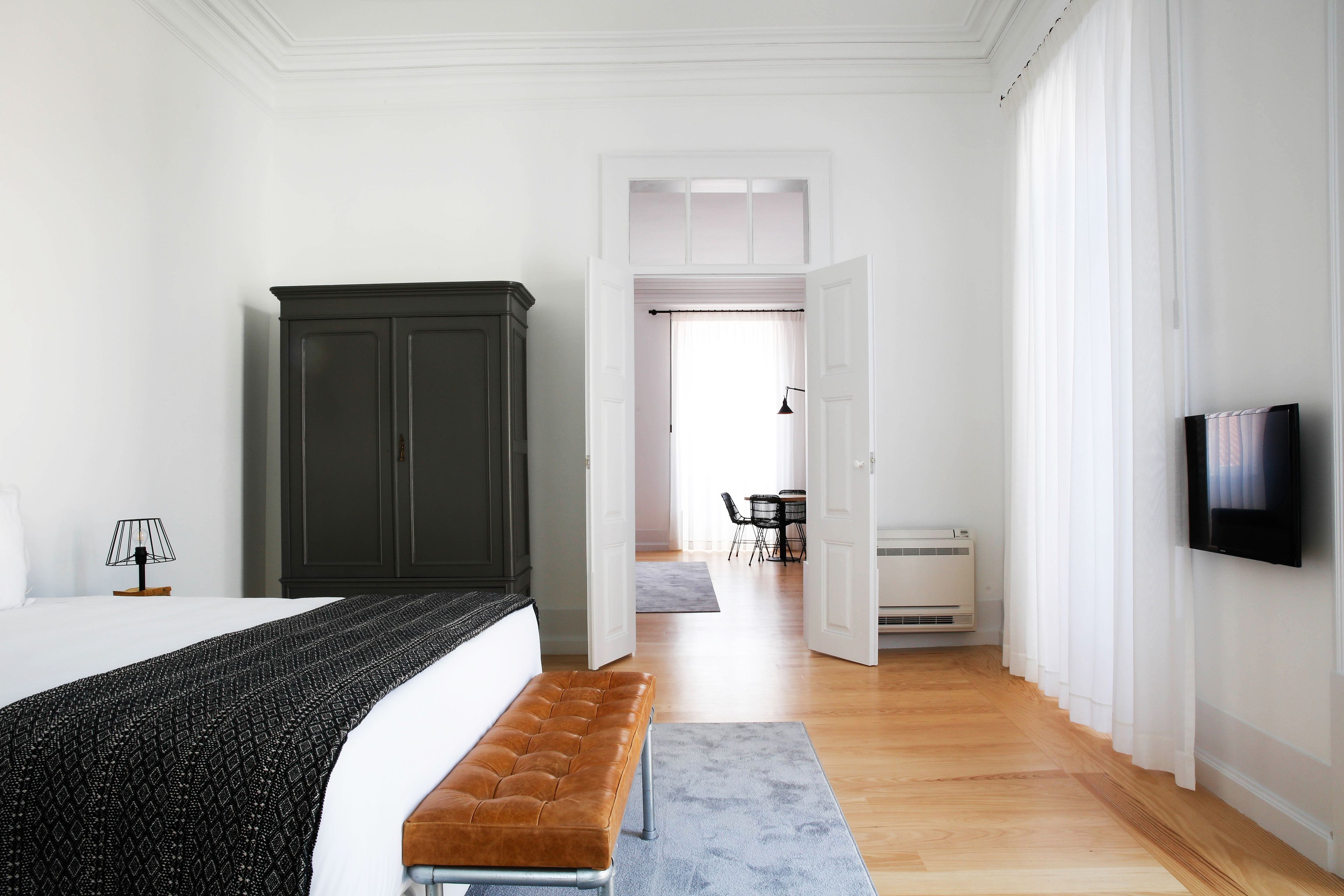 A bedroom with a bed, a bench, a wardrobe, and a television.