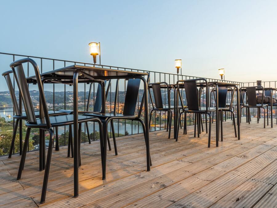 A terrace with tables and chairs, overlooking a river and cityscape.