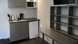 A compact kitchenette with a microwave, coffee maker, and a small refrigerator. There is a dining table with a chair and a TV mounted on the wall. - Smartappart Troyes (Troyes)