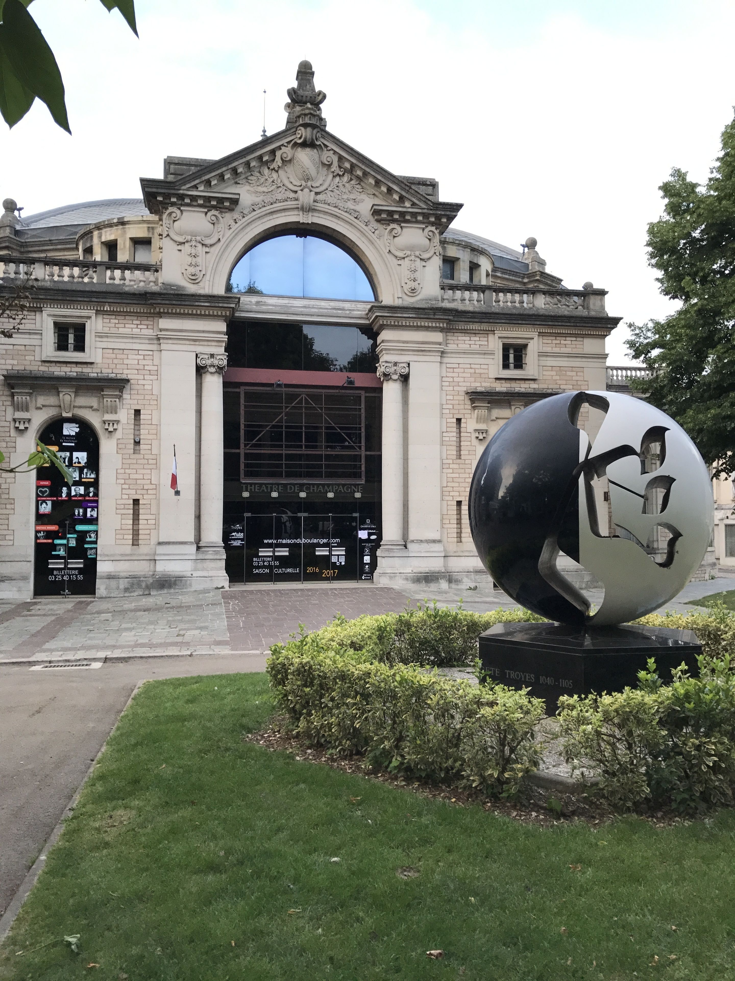 A historic building with a grand entrance, a large spherical sculpture in front, and a well-maintained lawn.