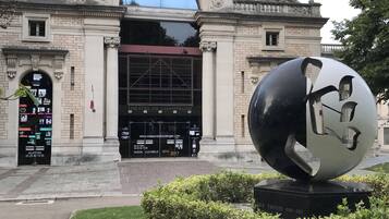 A historic building with a grand entrance, a large spherical sculpture in front, and a well-maintained lawn.
