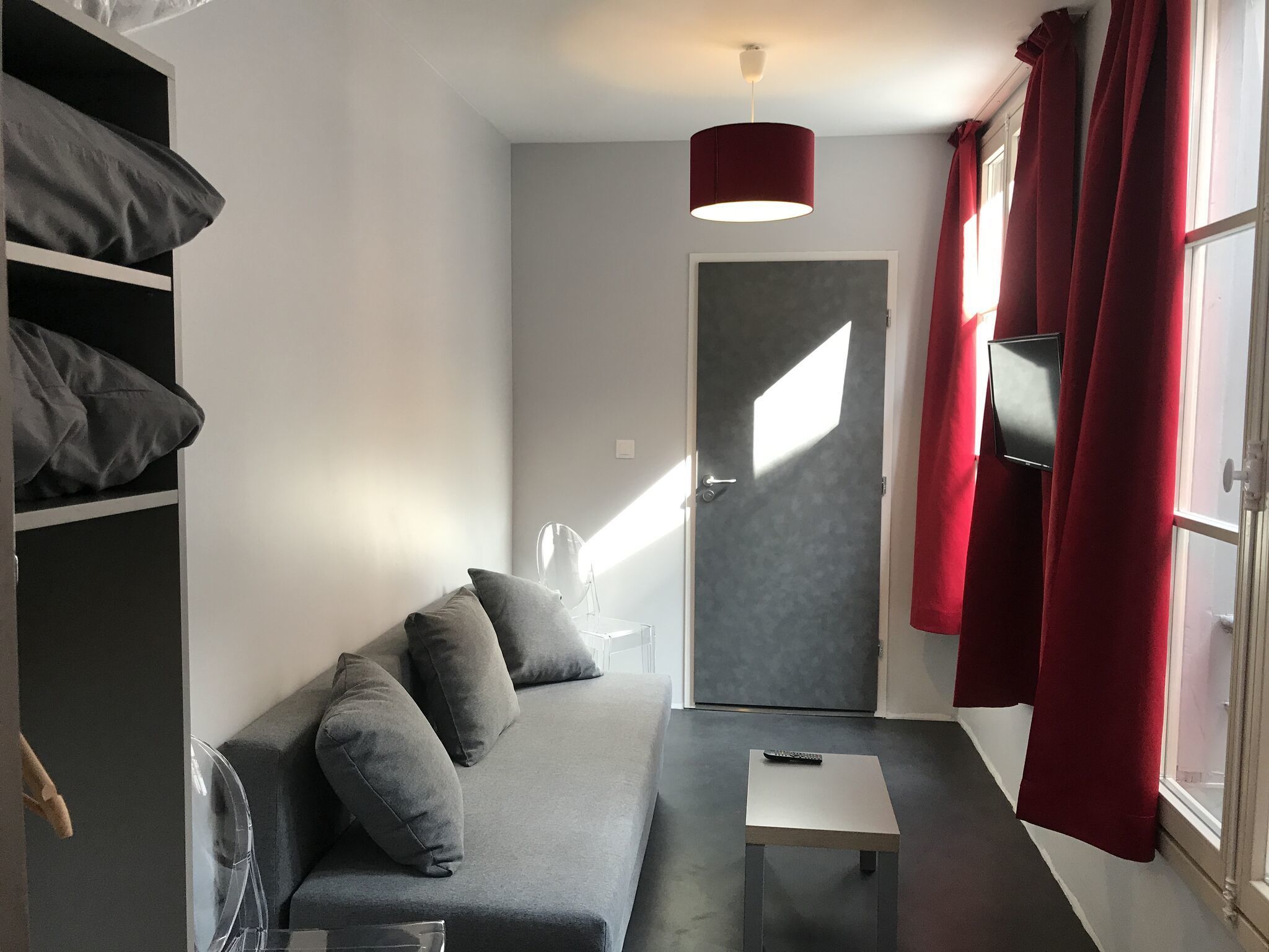 Un espacio habitable moderno y compacto con un sofá gris, una mesita y un televisor montado en la pared.