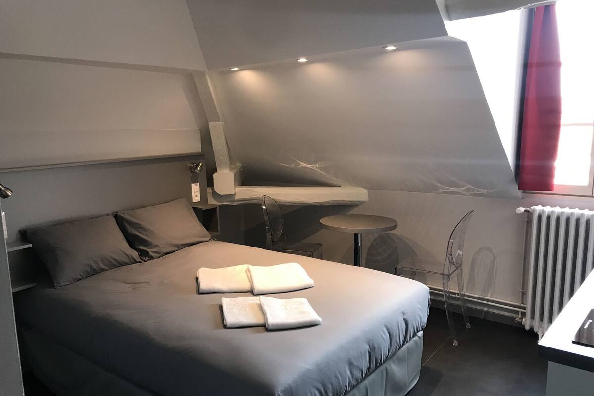 A modern bedroom with a large bed, a small desk, and a window with curtains.
