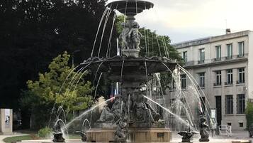 Una fuente de varios niveles con chorros de agua, rodeada por un muro bajo y pequeños arbustos.