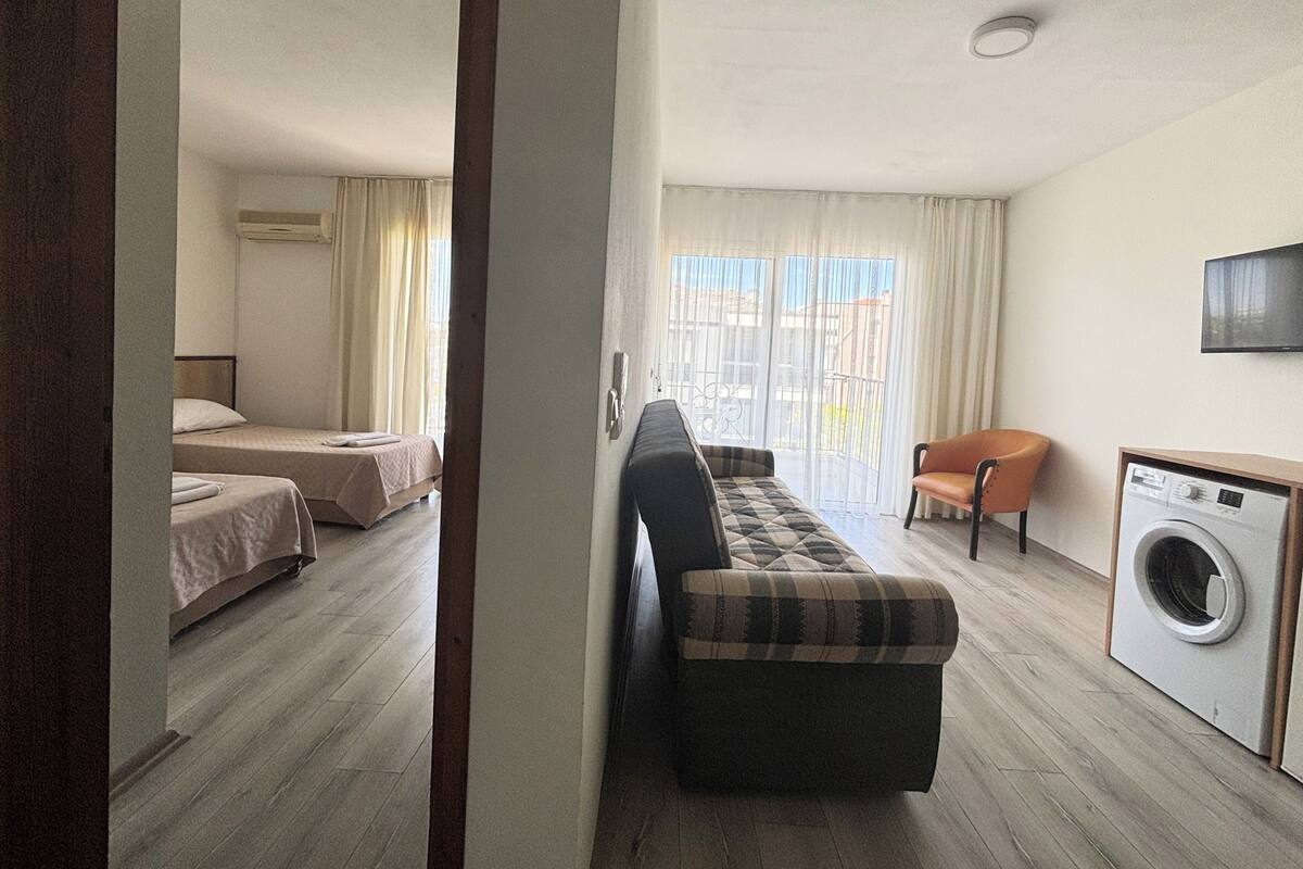 Una habitación de hotel con cama, sofá, sillón, lavadora y televisor.