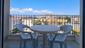 A balcony with a round table and two chairs, offering a view of buildings and a clear sky. - Fora Apart Otel (Cesme)