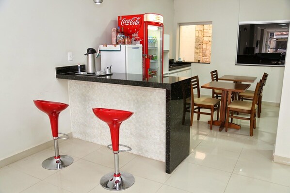 A kitchen with a bar area, two red bar stools, a dining table with chairs, and a refrigerator. - Big Hotel (Araguari)