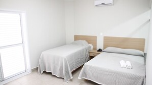Una camera d'albergo con due letti singoli, un comodino con una lampada e una finestra con tende.