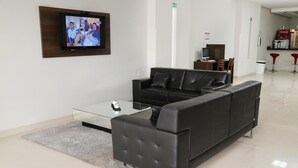 Una hall moderna con un divano in pelle nera, un tavolino in vetro e una televisione a schermo piatto montata a parete.