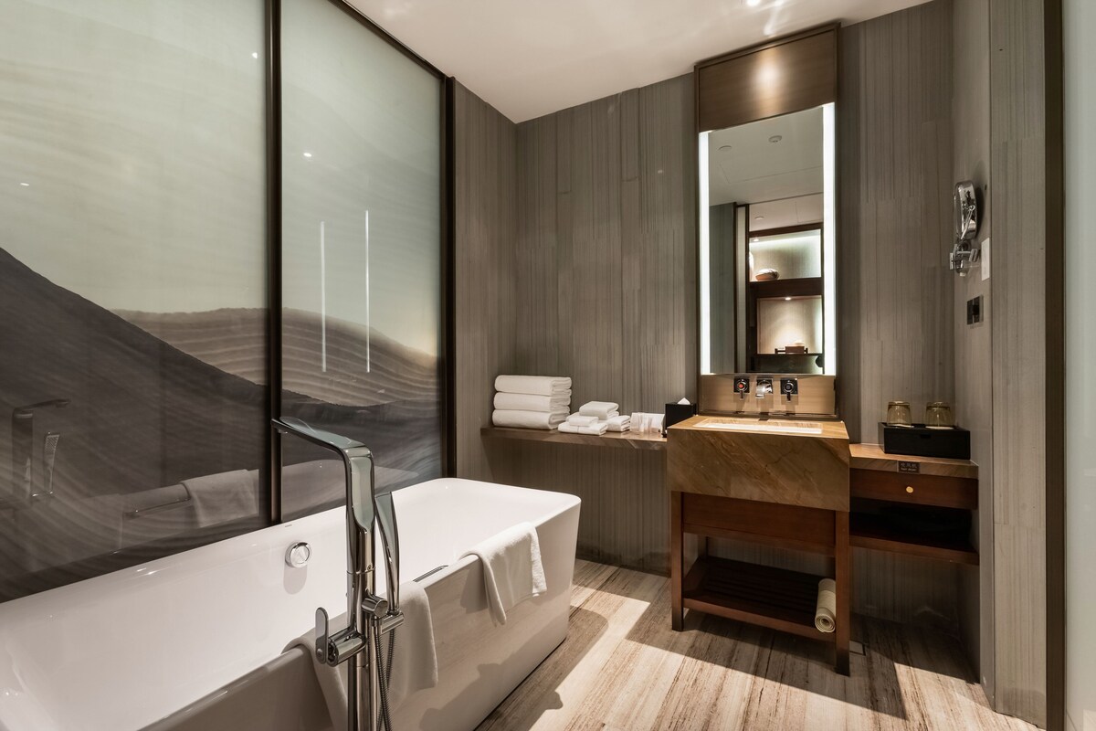 A modern bathroom with a large bathtub, a wooden vanity, and a mirror.
