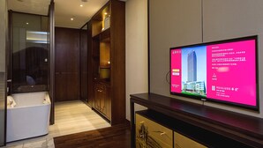 Habitación de hotel con un televisor de pantalla plana grande montado en la pared, un armario de madera y zona de ducha con mampara de vidrio.