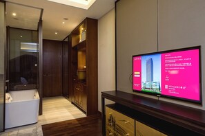 A hotel room with a large flat-screen TV mounted on the wall, a wooden wardrobe, and a glass-enclosed shower area. - HUALUXE Wuxi Taihu by IHG (Wuxi)