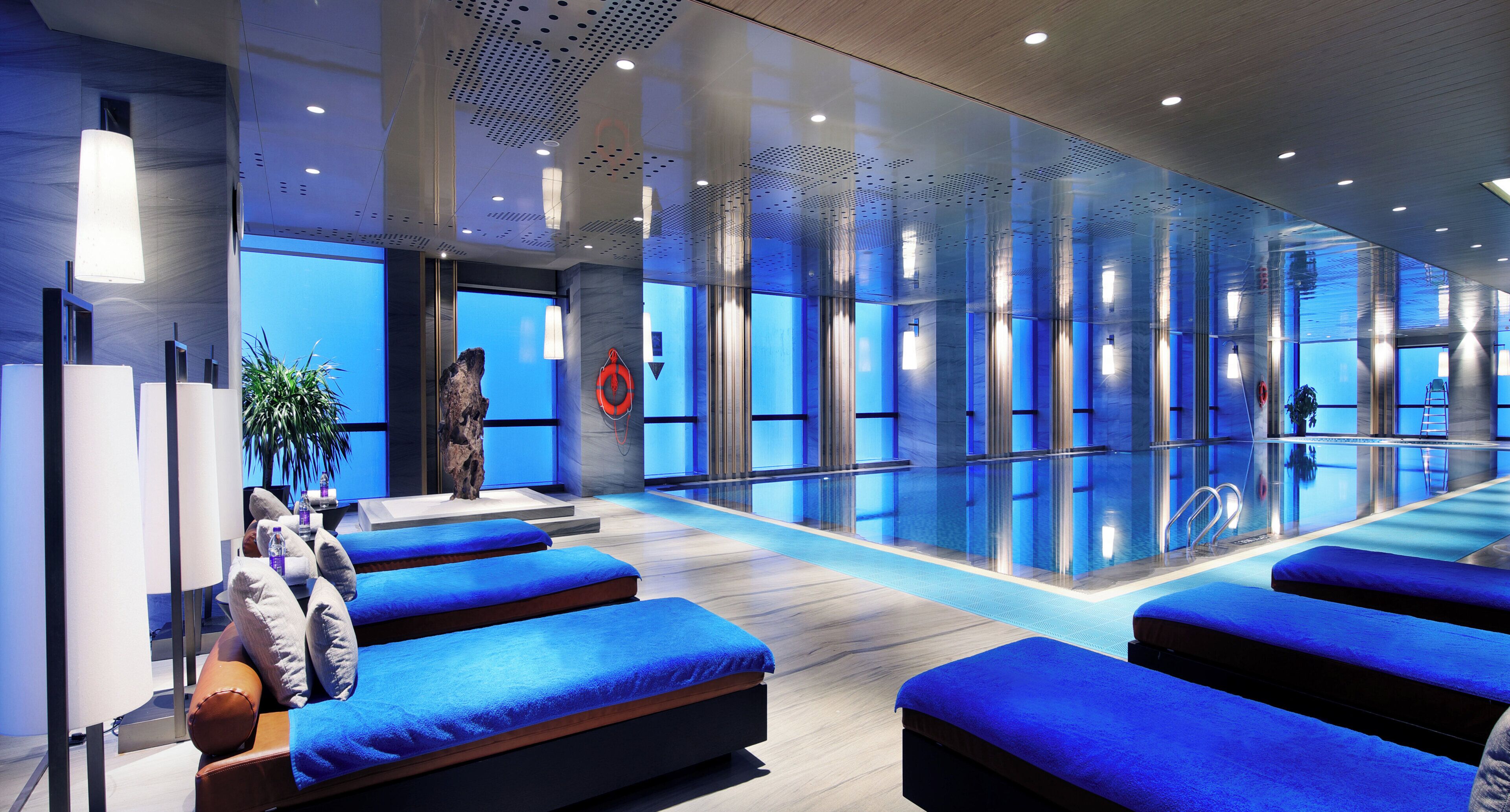 A modern spa area with a pool, blue cushioned seating, and a clear glass wall.