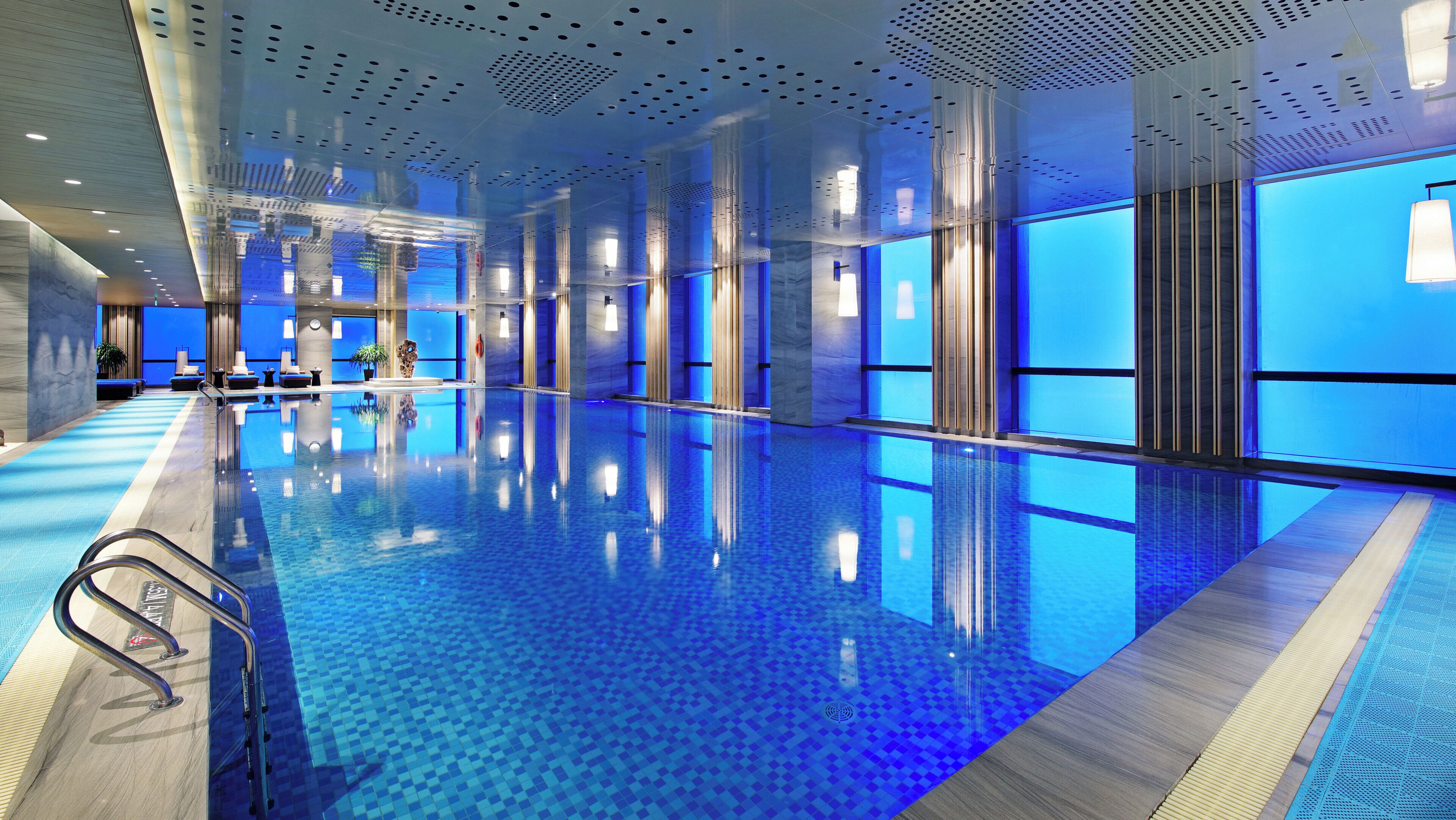 Piscina interior moderna com água cristalina, extensa área ao redor da piscina e teto com design perfurado exclusivo.