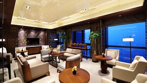 Un moderno hall de hotel con una amplia zona de estar, un bar y grandes ventanales que ofrecen vistas.