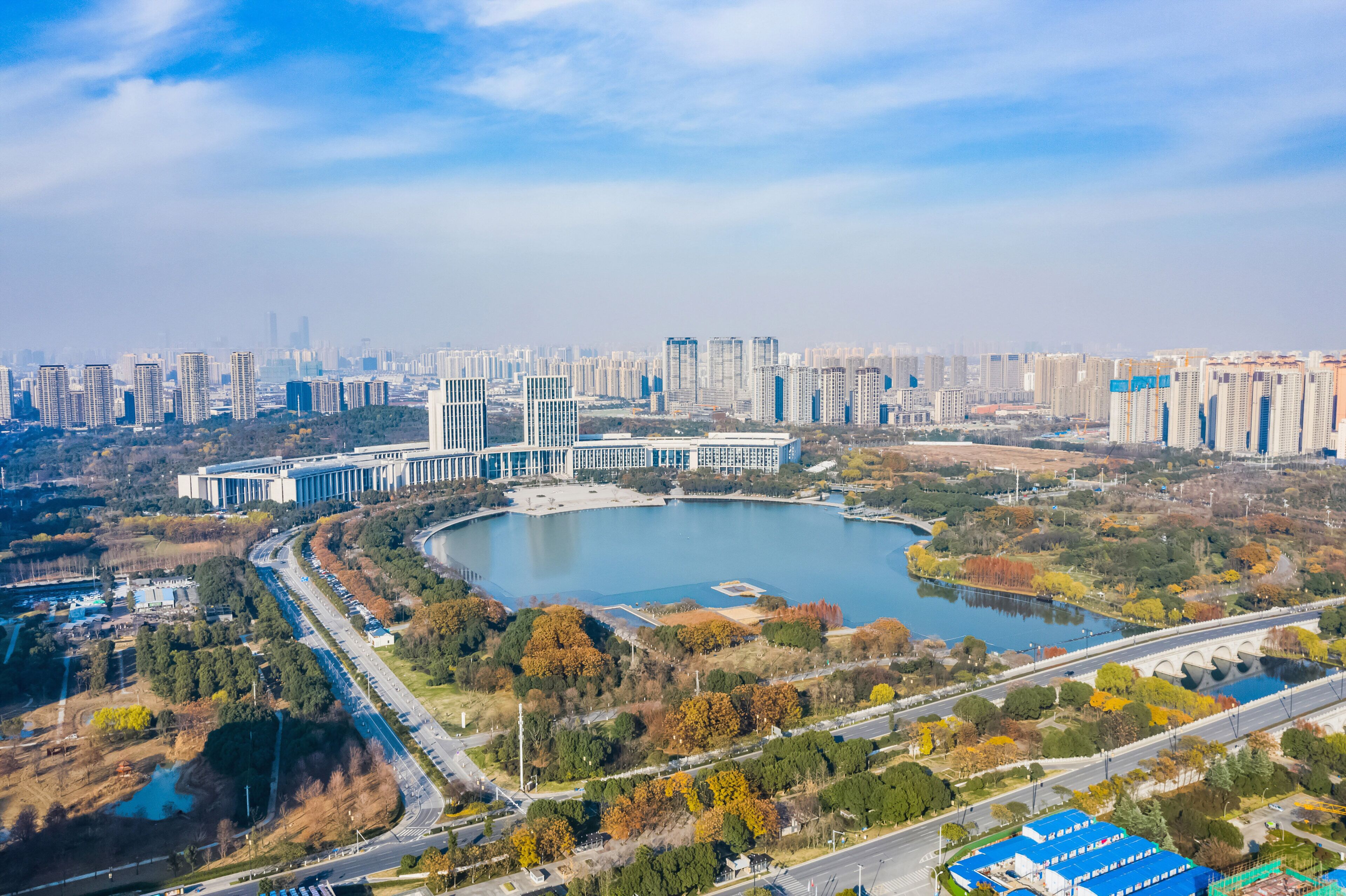 A cityscape with modern high-rise buildings, a large central park with a lake, and a bridge connecting different areas.