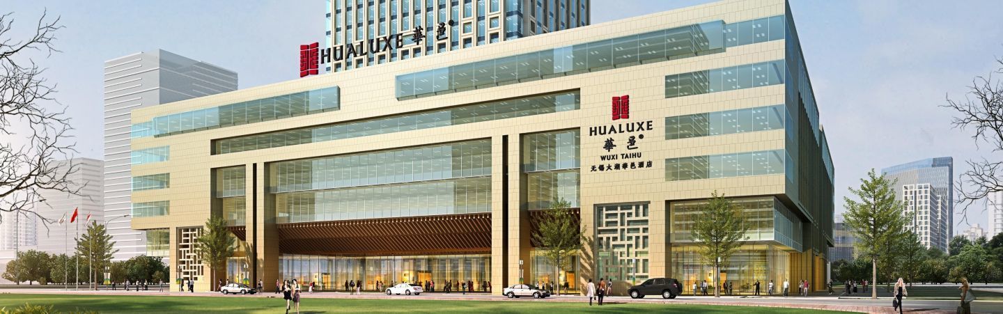 A modern building with a large glass facade, signage for Hualuxe Wuxi Taihu, and a covered entrance.